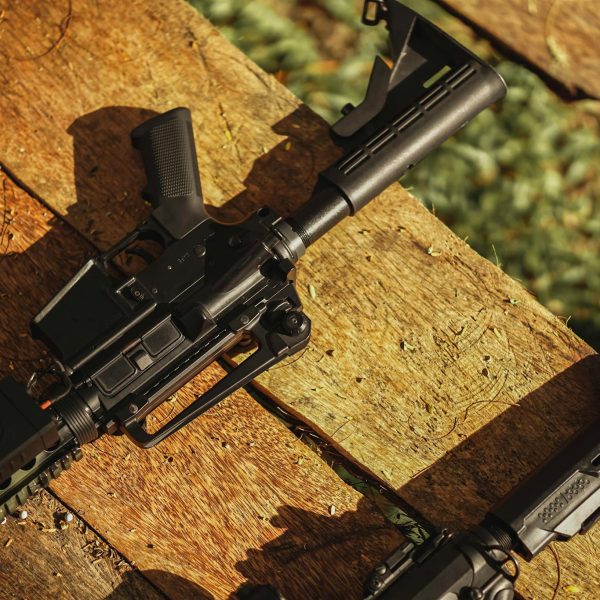 AR-style rifle displayed on wooden planks in natural light, showcasing tactical features.